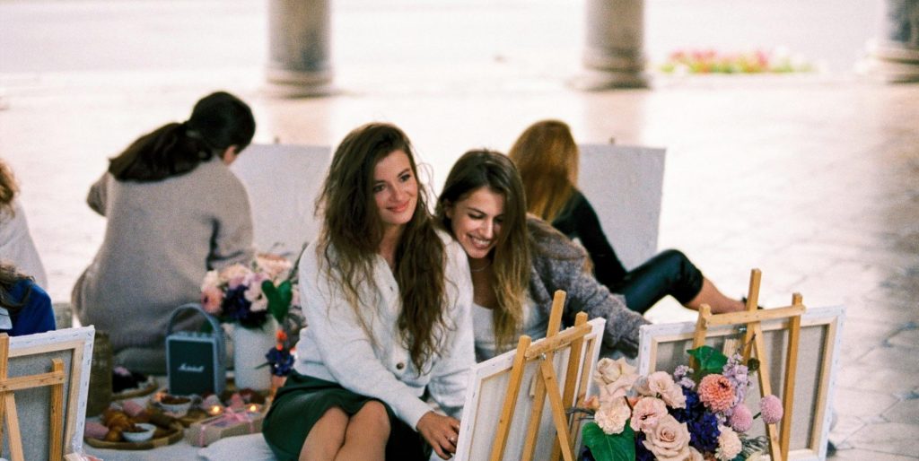 A group of women enjoying an art session in an outdoor pavilion with columns.
