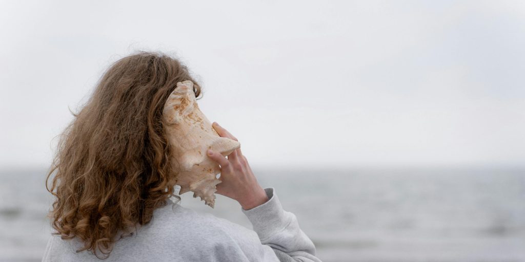 A young woman listens to a seashell by the ocean. Peaceful coastal scene.