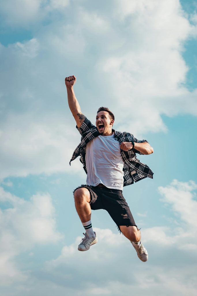 pexels-photo-2923156-2923156 A joyful young man jumps midair with clouds and blue sky in the background, exuding energy and freedom.