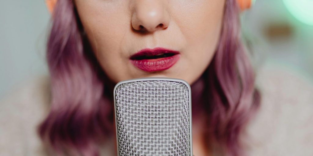 Close-up of a woman with purple hair speaking into a microphone.